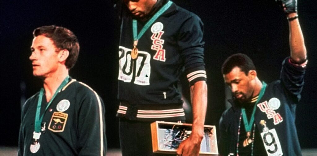 ohn Carlos y Tommie Smith con sus brazos en alto.